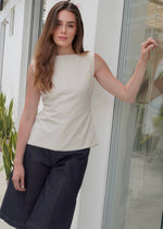 Woman wearing a white sleeveless linen top and jeans  standing indoors.