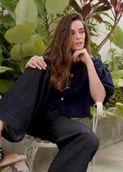 Woman sitting on a chair with plants in the background. Navy Blue linen blouse